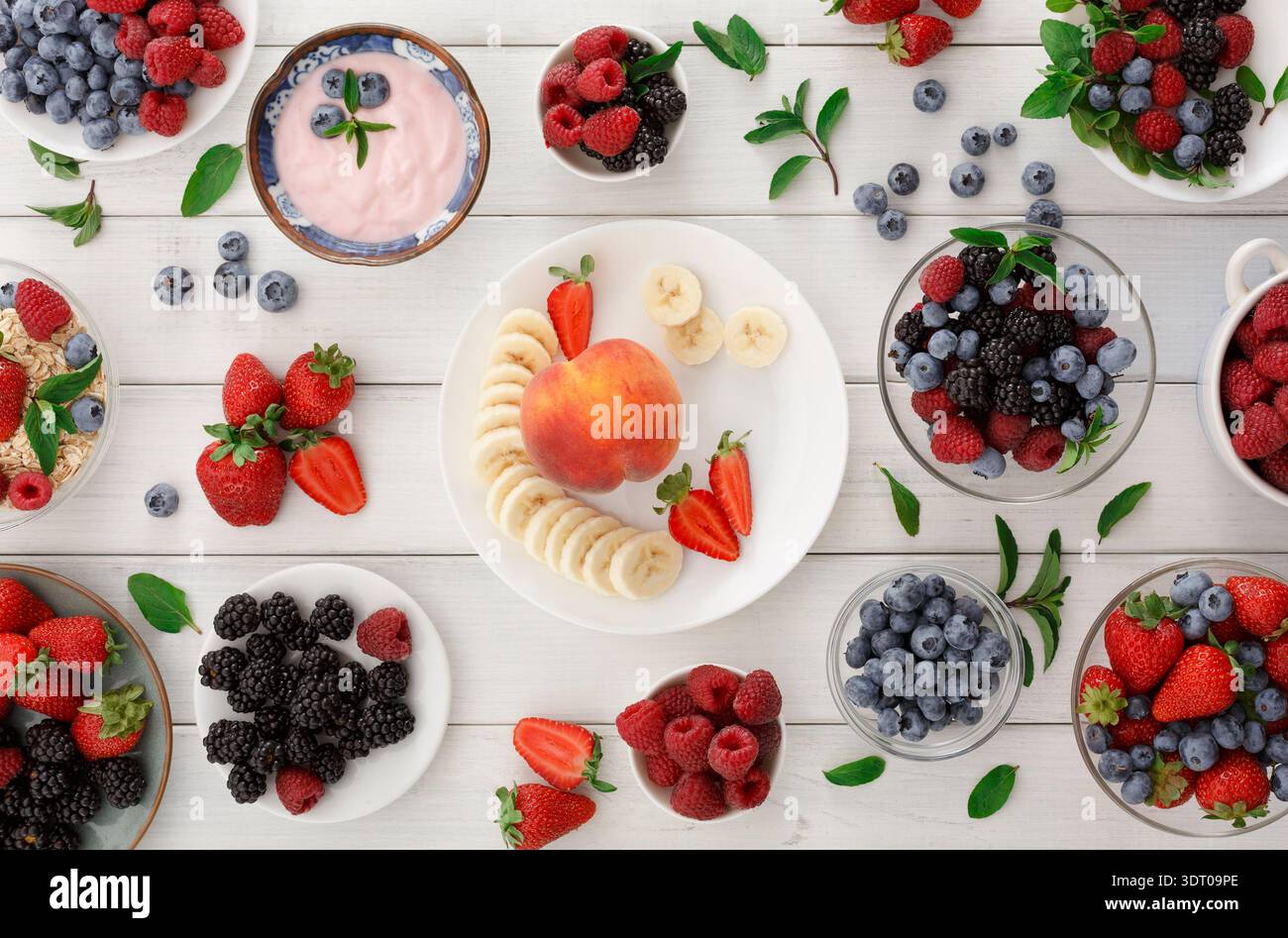 Collage di frutta colorata su un tavolo bianco con bacche, banane e ciotole di yogurt Foto Stock