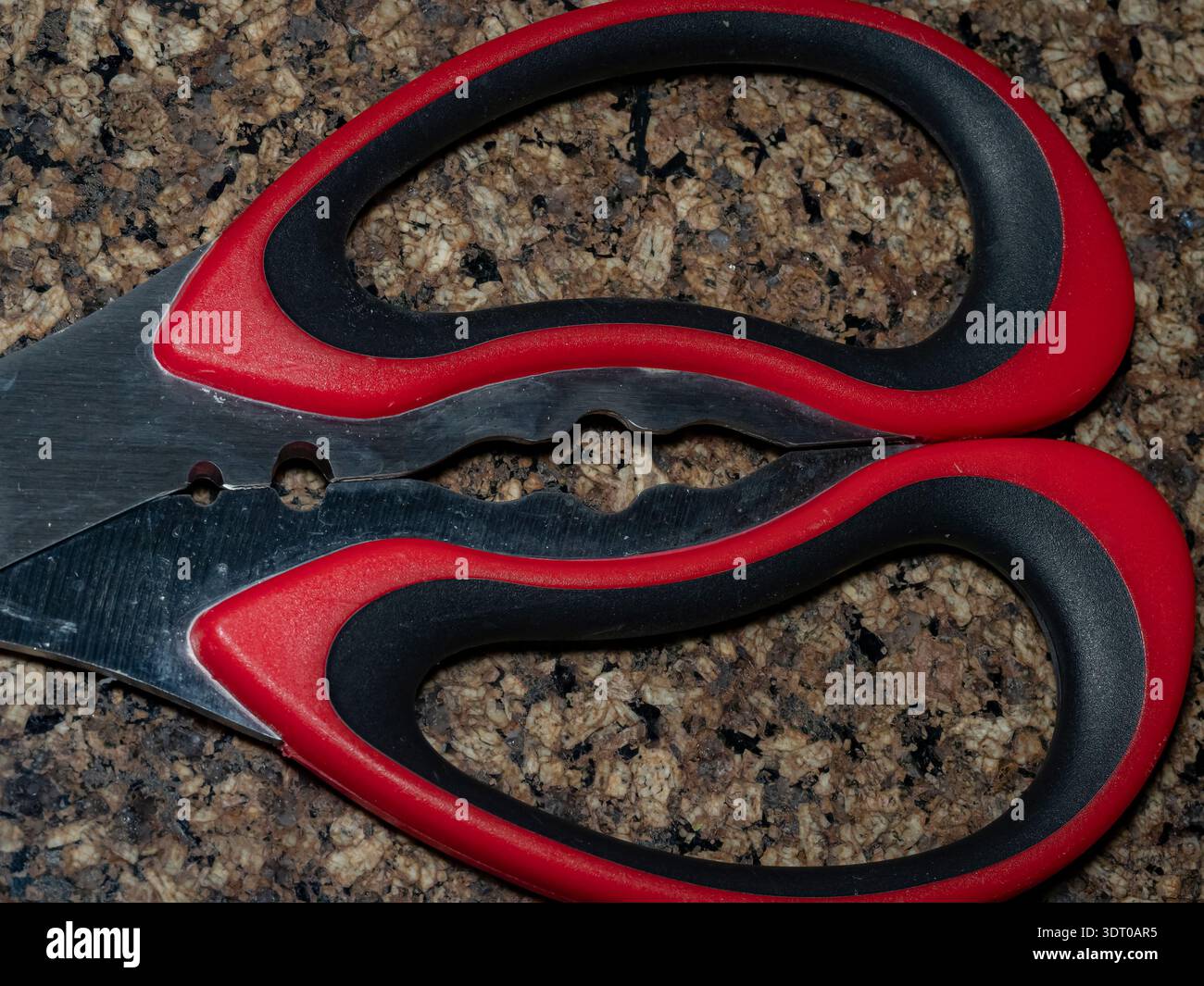 Primo piano di forbici rosse e nere sul piano di lavoro in granito, simboleggiando gli utensili domestici, la sicurezza e la maestria artigianale Foto Stock