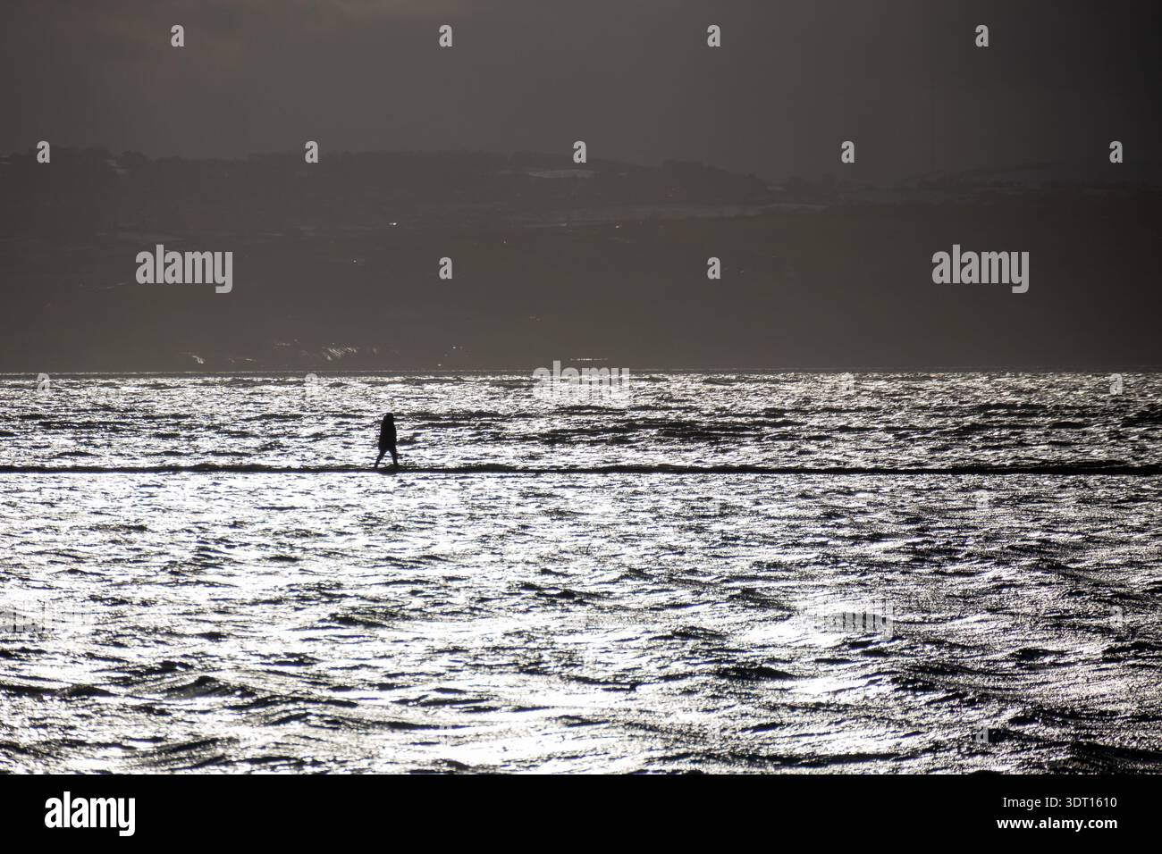 Silhouette di una persona che cammina su un sentiero pavimentato intorno al lago marino Foto Stock