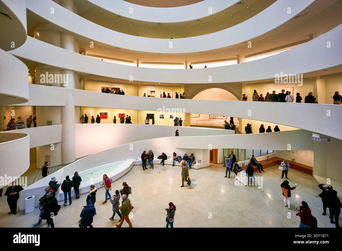 Molte persone camminano attraverso gli ampi spazi del Solomon R. Guggenheim Museum di Manhattan. La grafica viene visualizzata sulle pareti per la visualizzazione. Foto Stock