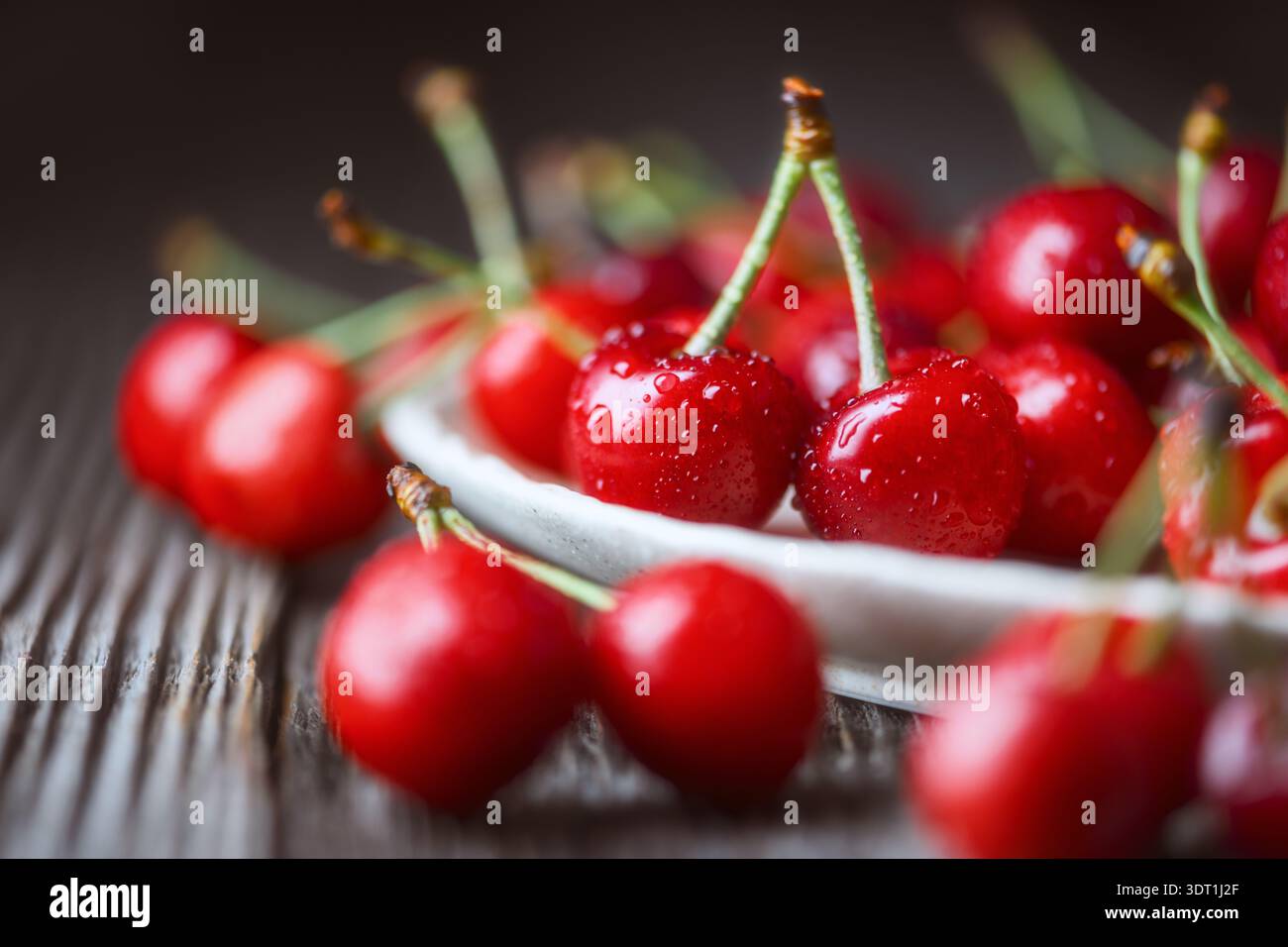 Ciliegie mature disposte in piatto di ceramica su una superficie di legno. Frutta rossa lucida fresca, luce naturale, raccolta biologica Foto Stock