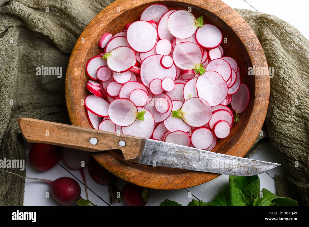 Insalata di ravanello in un recipiente di legno con panno di lino e coltello rustico. Verdure biologiche per slow food e atmosfera da cucina rustica Foto Stock