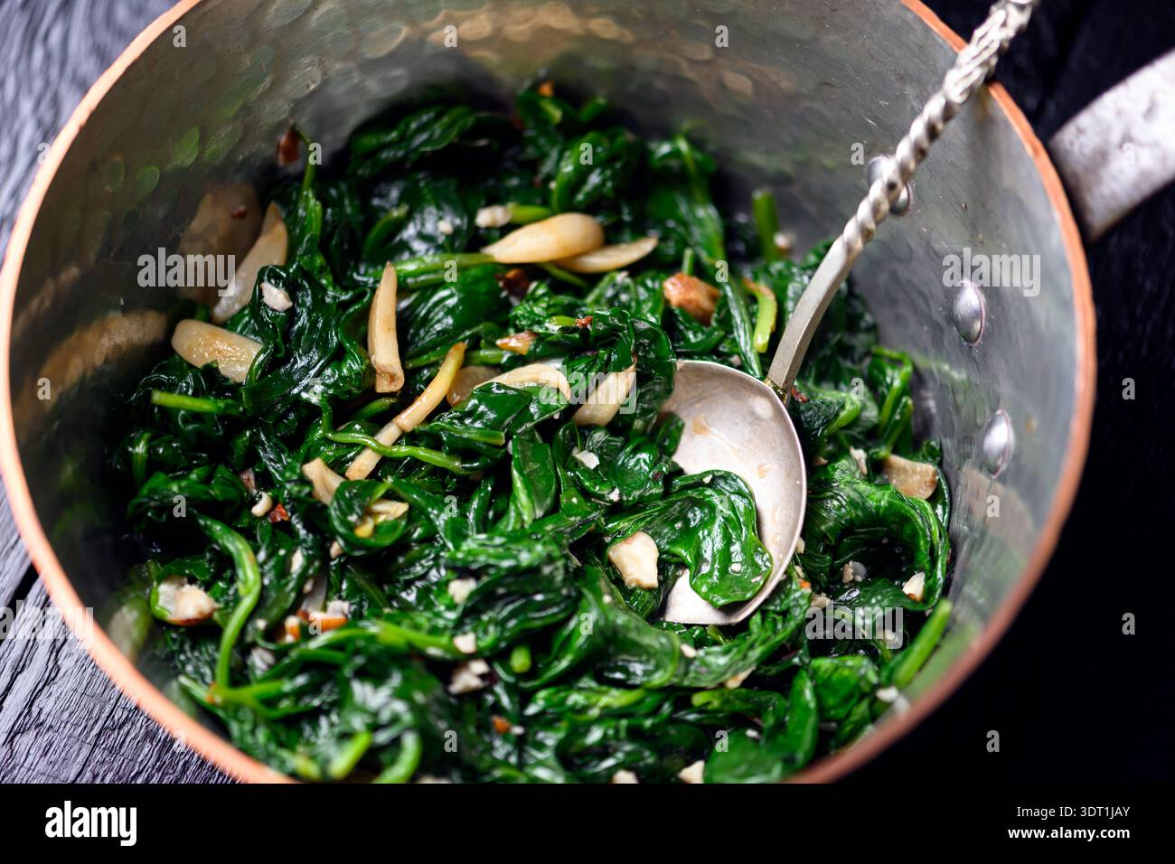 Salta di spinaci preparati in pentole in rame con cucchiaio su fondo in legno testurizzato. Utensili da cucina artigianali, ricetta fresca e concetto di stile di vita sano Foto Stock