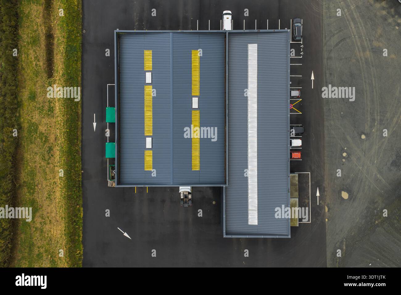 Vista aerea di un edificio con strisce gialle sul tetto che contrastano con l'asfalto scuro e l'erba verde, Tréglamus, Bretagne, Francia. Foto Stock