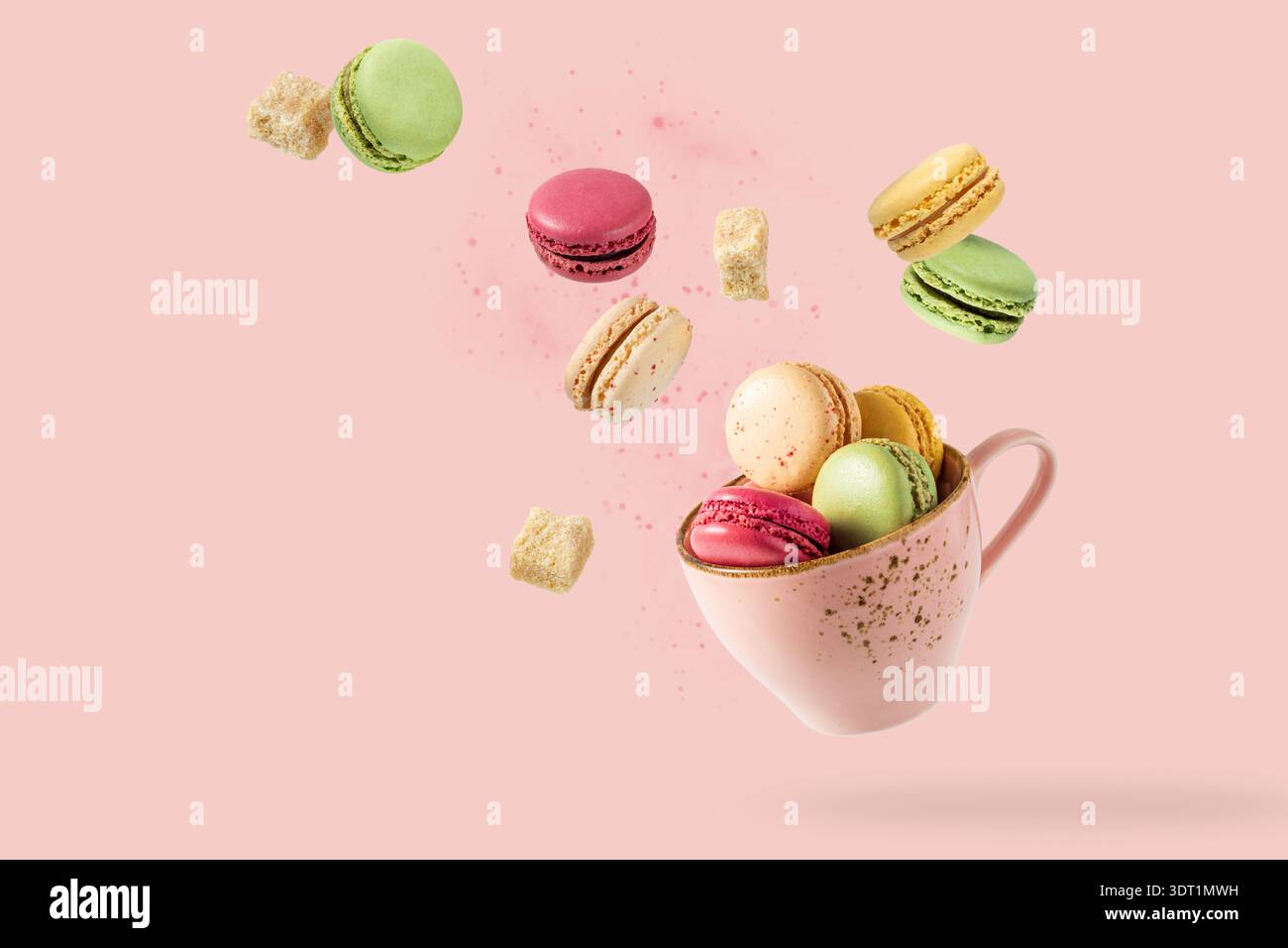 Biscotti dolci francesi colorati macaron macaron in tazza rosa vintage e cubetti di zucchero di canna che volano isolati su sfondo rosa chiaro. Scheda pasticceria Foto Stock