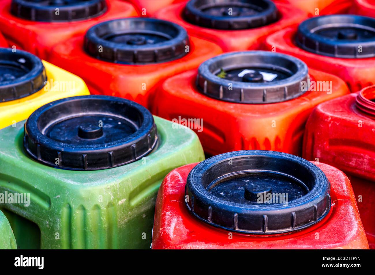 Primo piano di taniche in plastica colorata con tappi a vite neri in rosso, verde, arancione e giallo, scattate dall'alto. Foto Stock