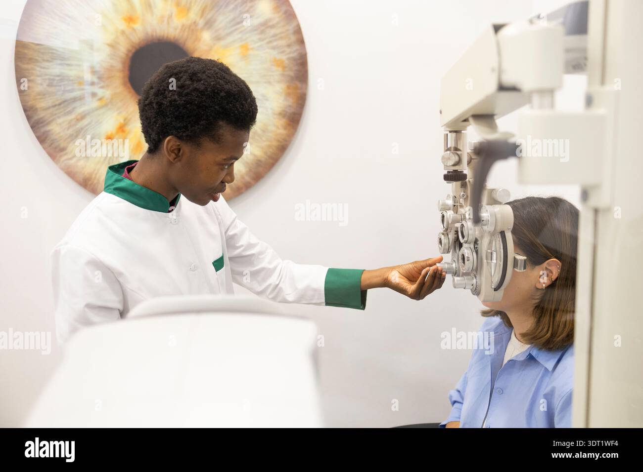 Un optometrista in un camice bianco conduce un esame oculare dettagliato utilizzando attrezzature specializzate in un ambiente clinico moderno con un modello a occhi grandi in Foto Stock