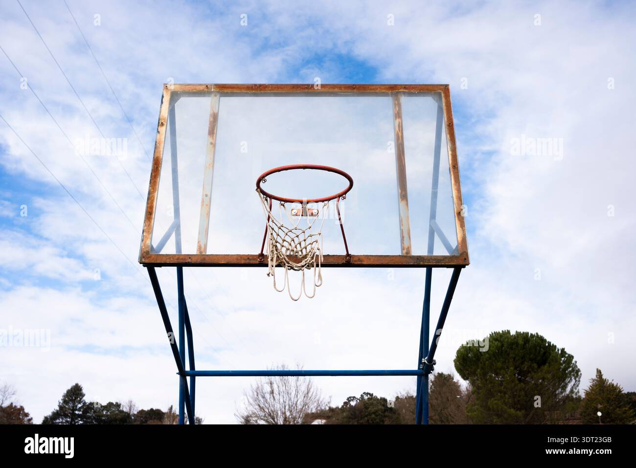Un canestro da basket vintage all'aperto si erge su un cielo blu limpido, con metallo arrugginito e una rete usurata, evocando un senso di nostalgia e senza tempo Foto Stock