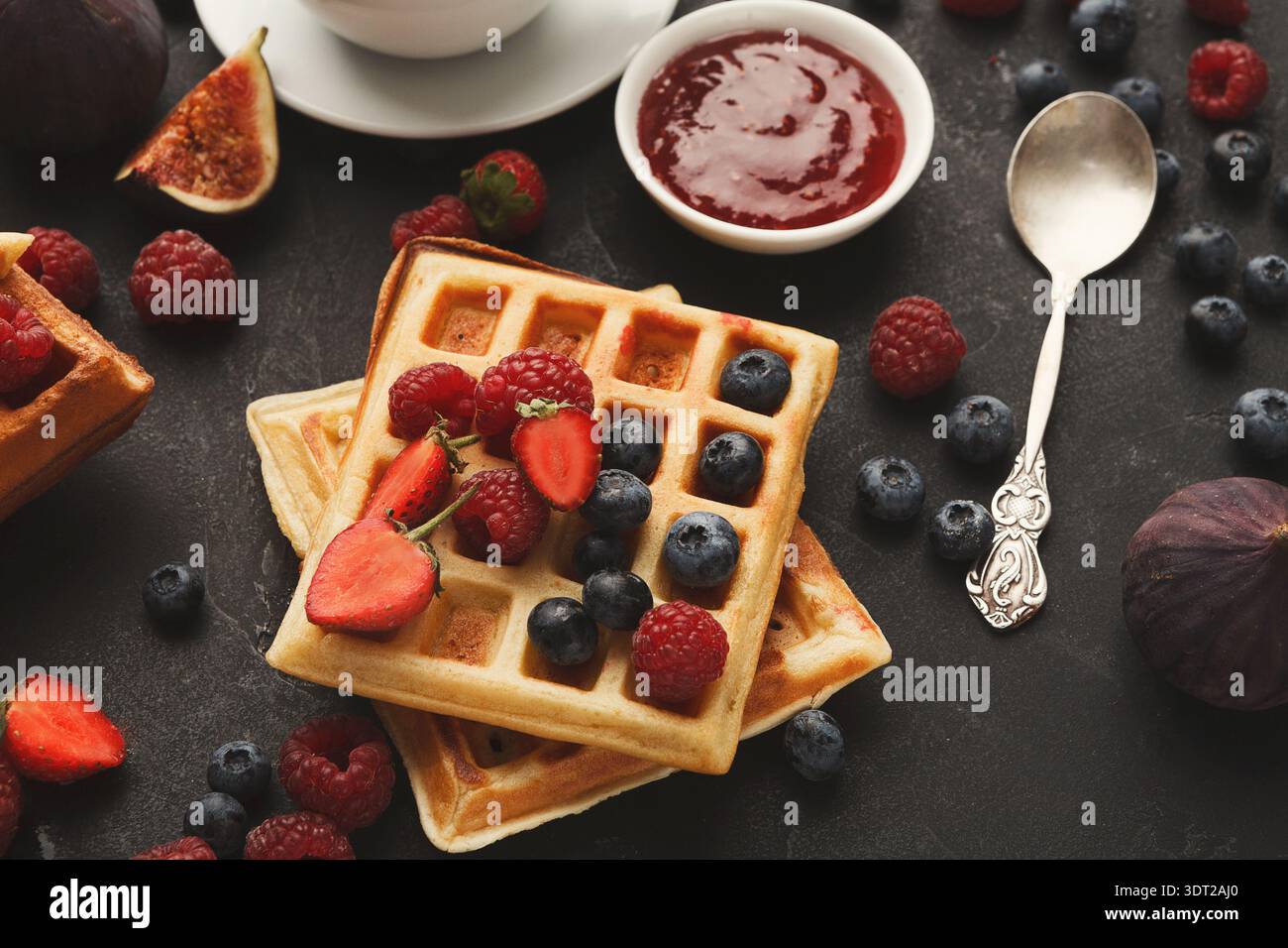 Waffle conditi con bacche fresche e marmellata su una superficie scura in un ambiente accogliente in cucina Foto Stock