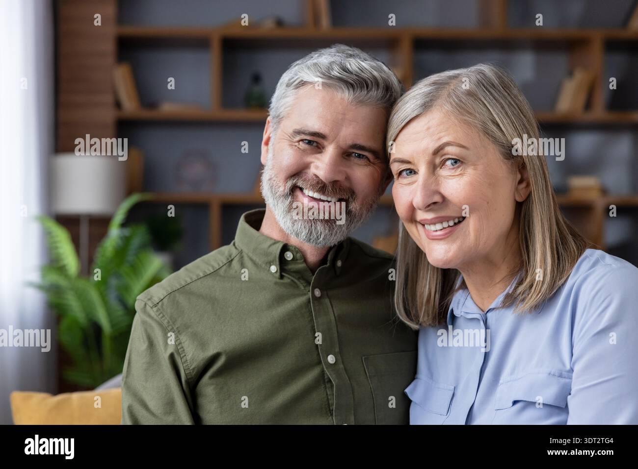 Coppia matura sorridente a casa che condivide un caldo abbraccio, irradiando amore, soddisfazione e compagnia nella loro vita quotidiana rilassata e pensione insieme Foto Stock