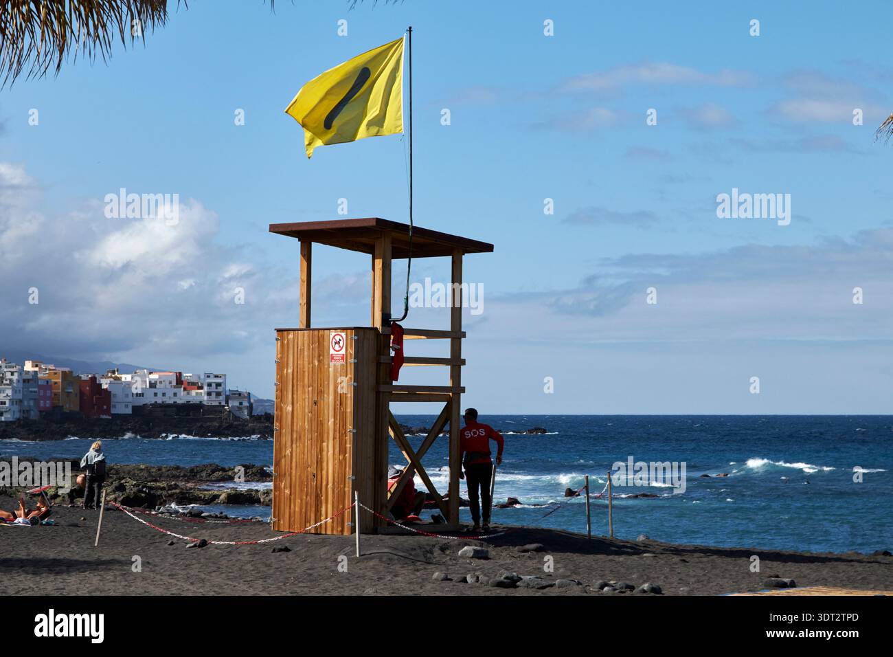 bagnino da spiaggia con torre che mostra una bandiera di avvertimento gialla con aggiunta di coloranti per le persone con cecità di colore puerto de la cruz tenerife cana Foto Stock