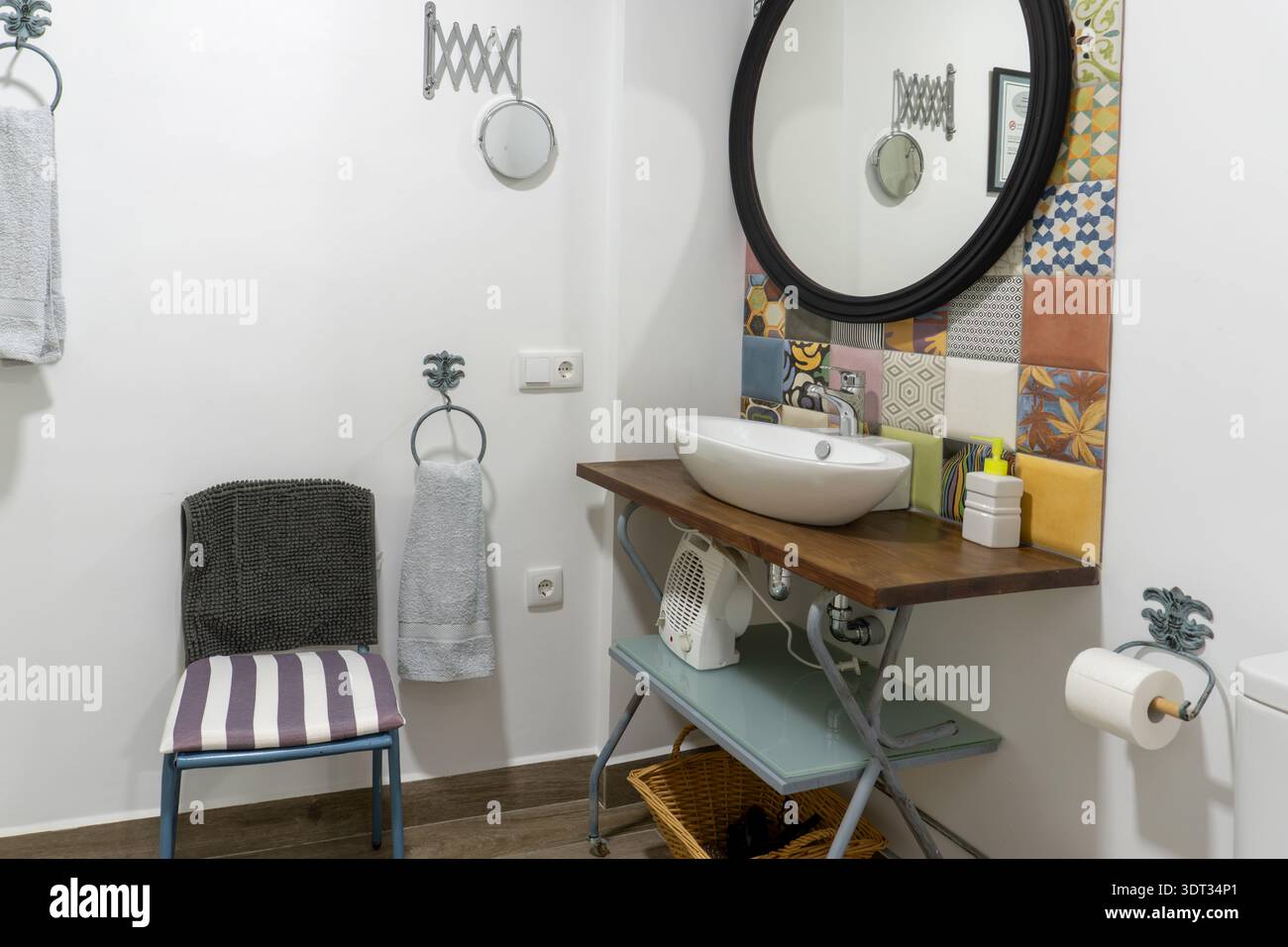 L'interno del bagno presenta un lavandino su un piano in legno rustico, abbinato a uno specchio rotondo e piastrelle decorative a motivi geometrici Foto Stock