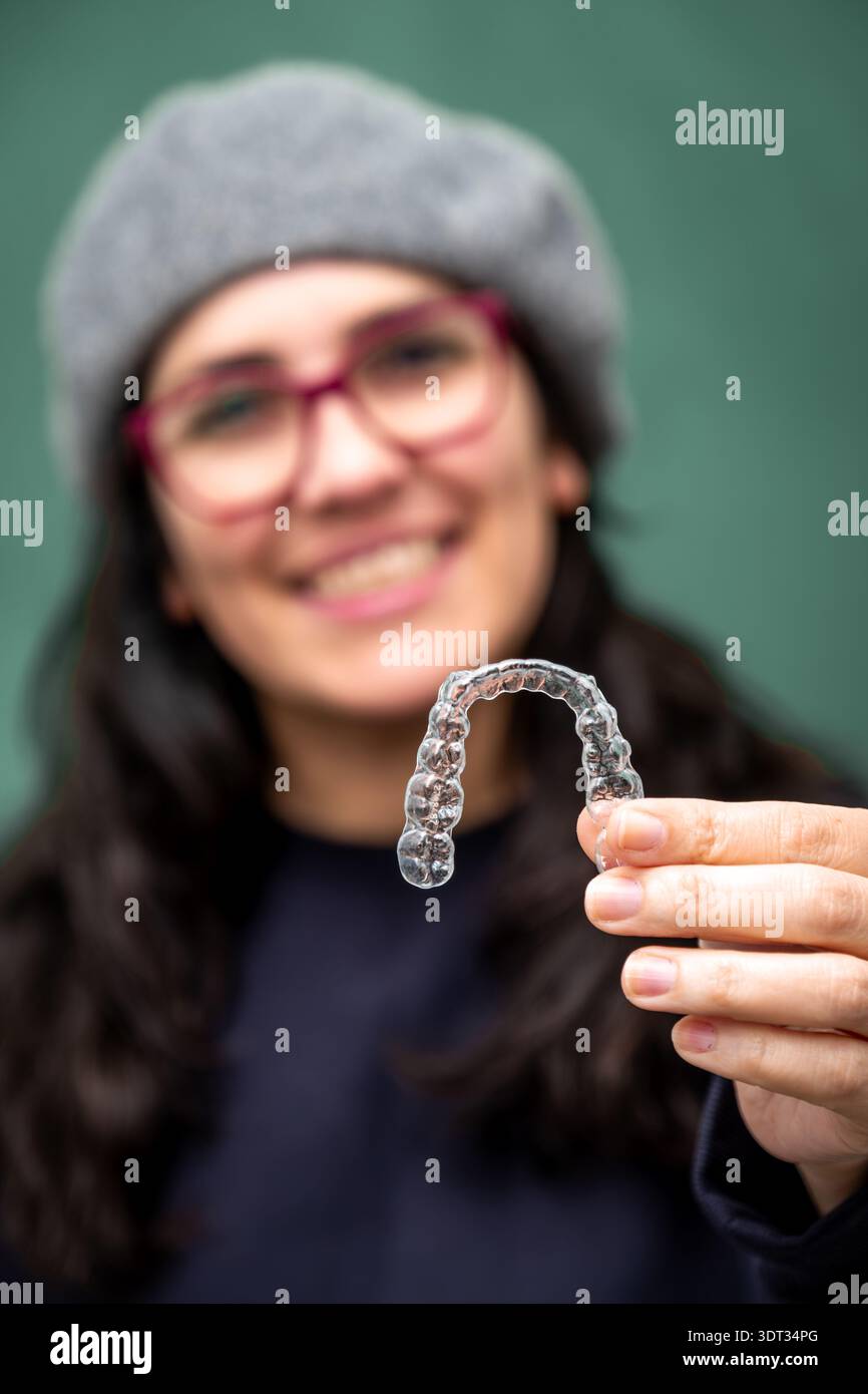 Donna sorridente che mostra un allineatore dentale trasparente, che rappresenta l'ortodonzia moderna e una sottile correzione del sorriso Foto Stock