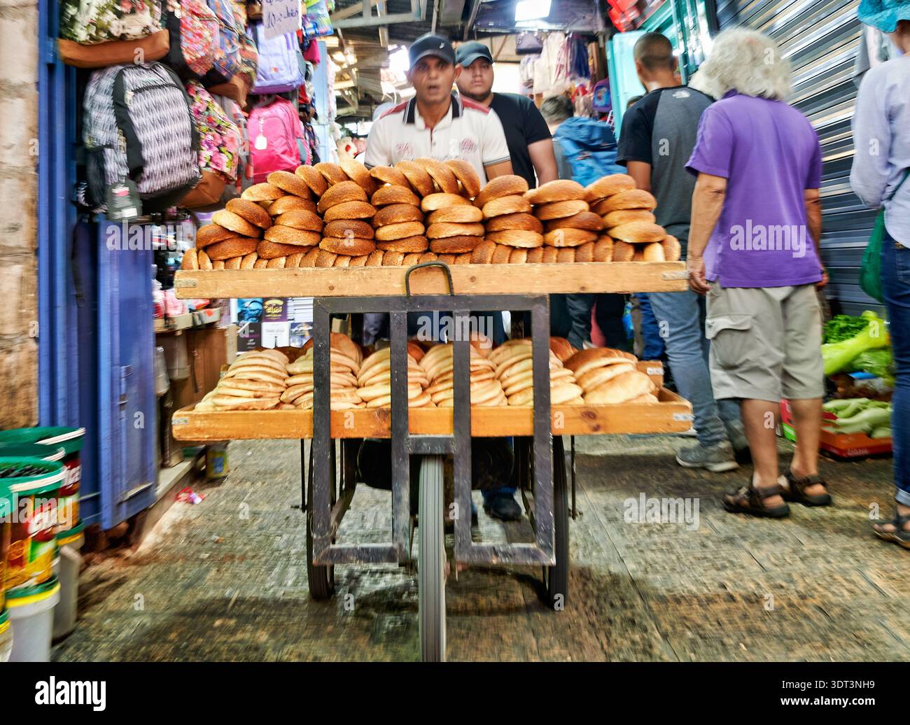 Un fornaio sposta il suo carro riempito di pane fresco attraverso le strade trafficate della città vecchia di Gerusalemme. La gente lo aggira mentre lavora. Foto Stock