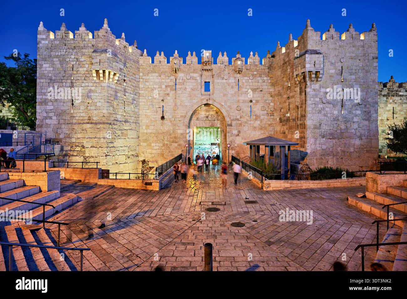 I visitatori si avvicinano alla porta di Damasco a Gerusalemme durante il tramonto mentre il cielo cambia colore. Le antiche pietre brillano dolcemente alla luce della sera. Foto Stock