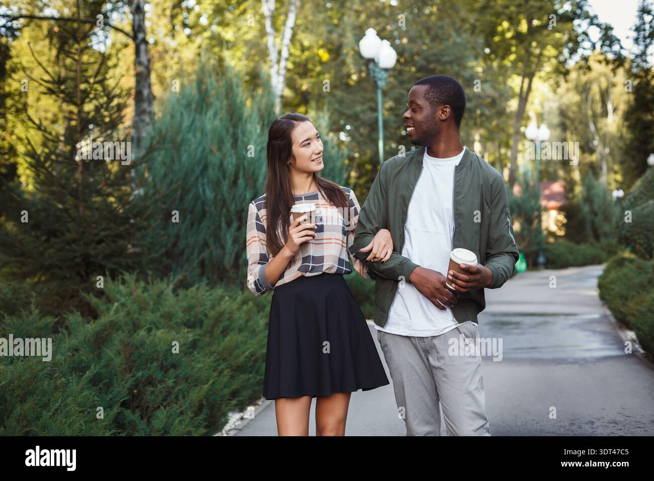 La coppia ama passeggiare in un parco tenendo tazze da caffè e sorridendo l'un l'altro Foto Stock
