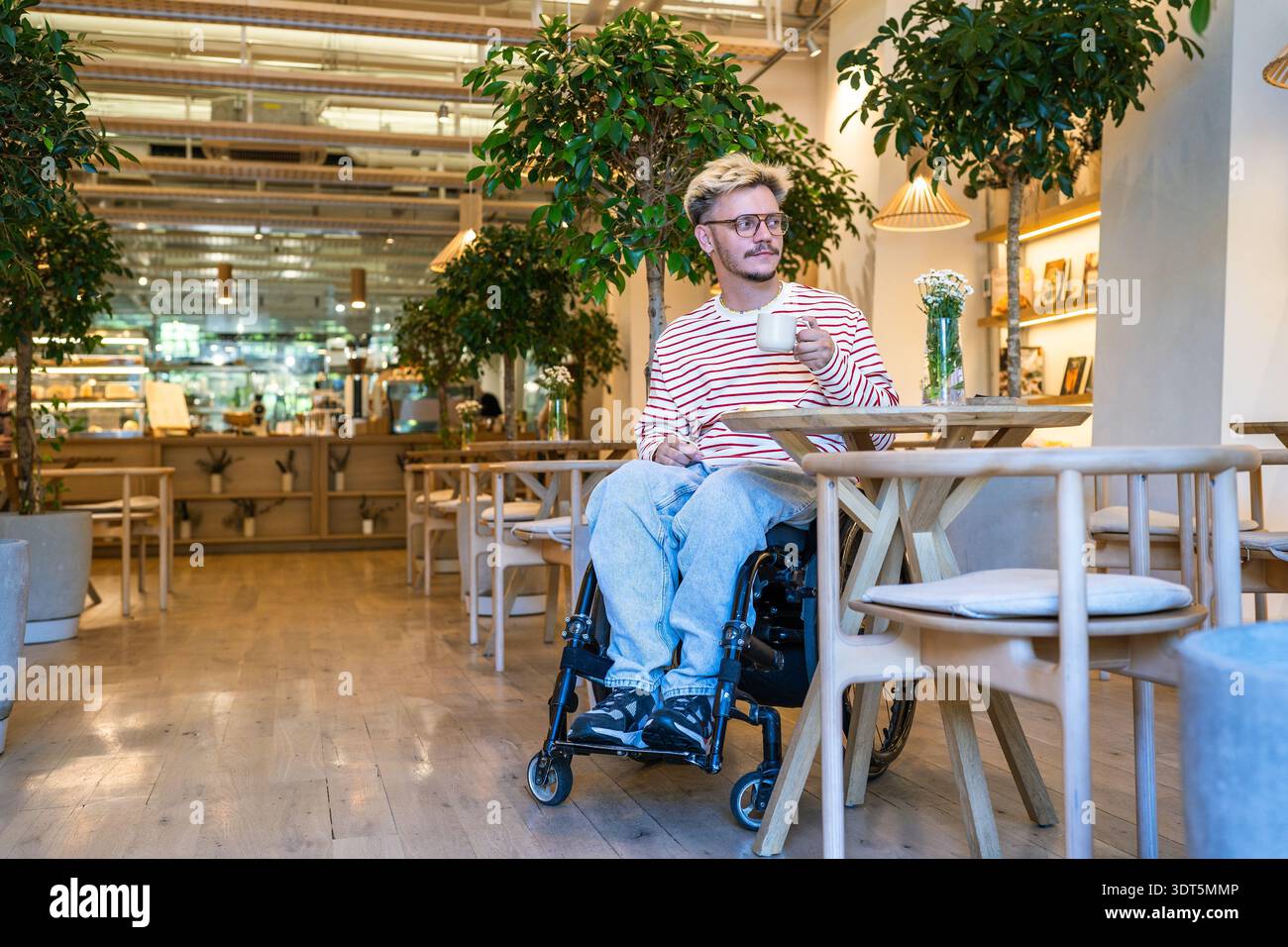 Rilassato uomo disabile positivo in sedia a rotelle che beve caffè in un caffè alla moda, rimanendo socialmente attivo. Foto Stock