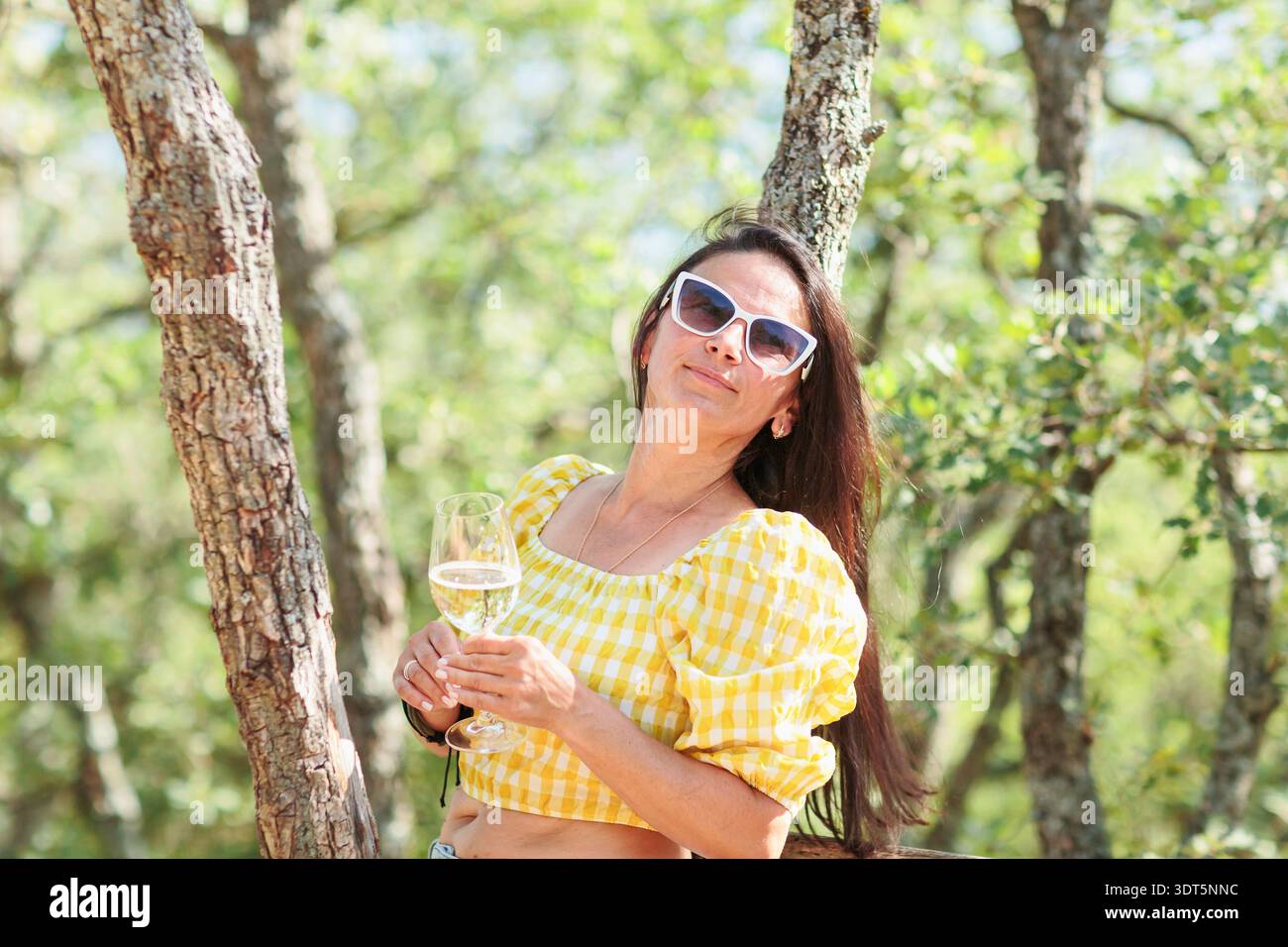 Donna matura e sicura di sé che si rilassa con vino bianco nella Sunny Forest Foto Stock
