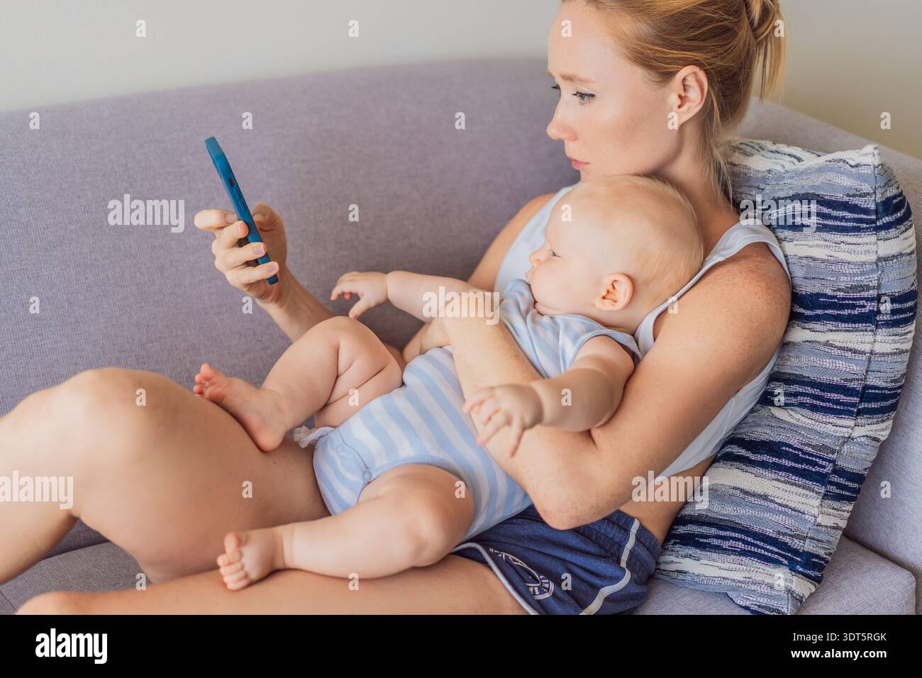 Il bambino seduto in grembo della madre mentre guarda il suo smartphone, emotivamente disconnesso. Scena simbolica che mostra l'impatto della distrazione dello schermo sui neonati Foto Stock