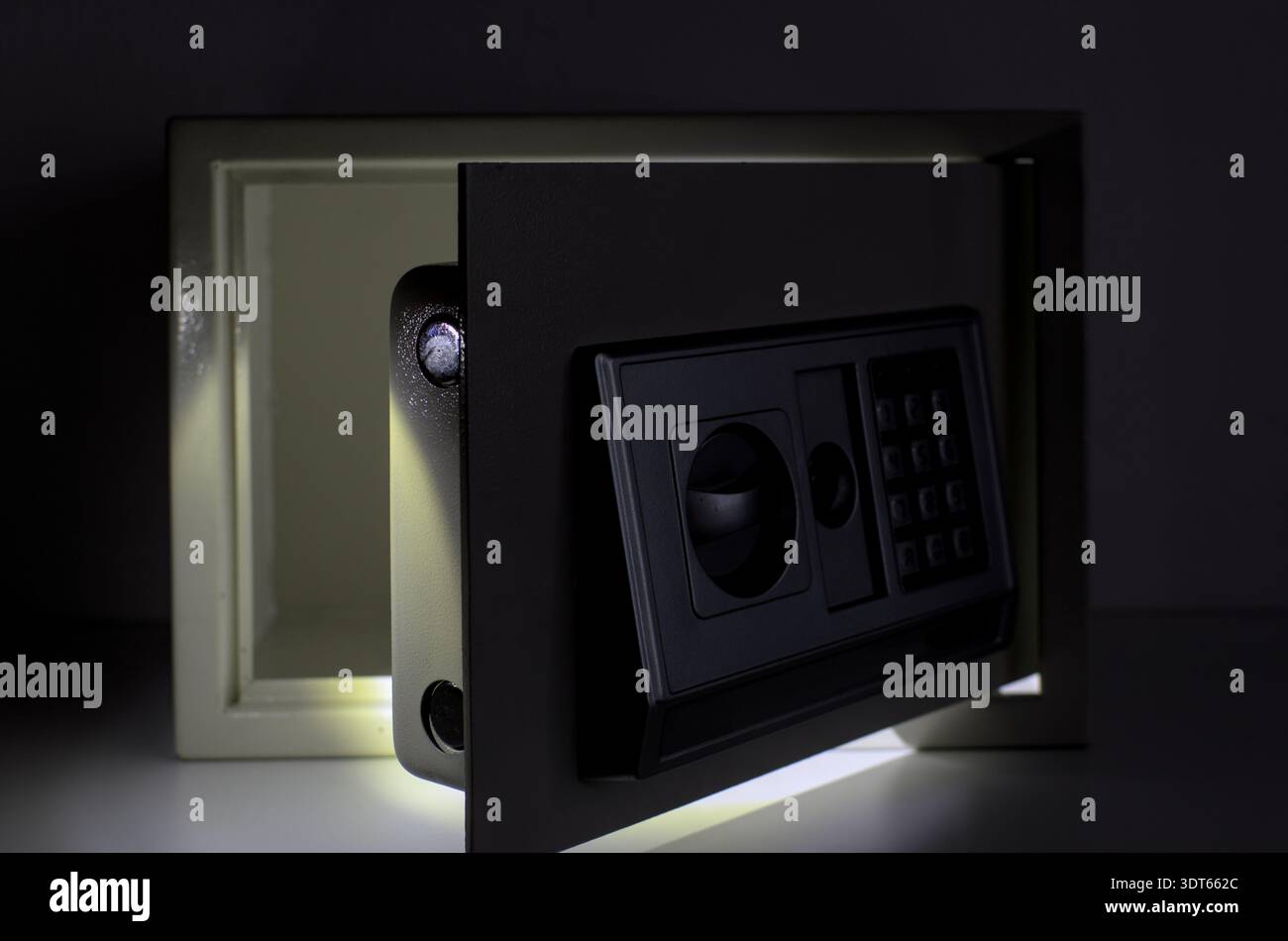 Piccola cassetta di sicurezza elettronica illuminata da un raggio di luce in una stanza buia. Concetto di mistero, risparmi nascosti, sicurezza domestica, protezione finanziaria Foto Stock