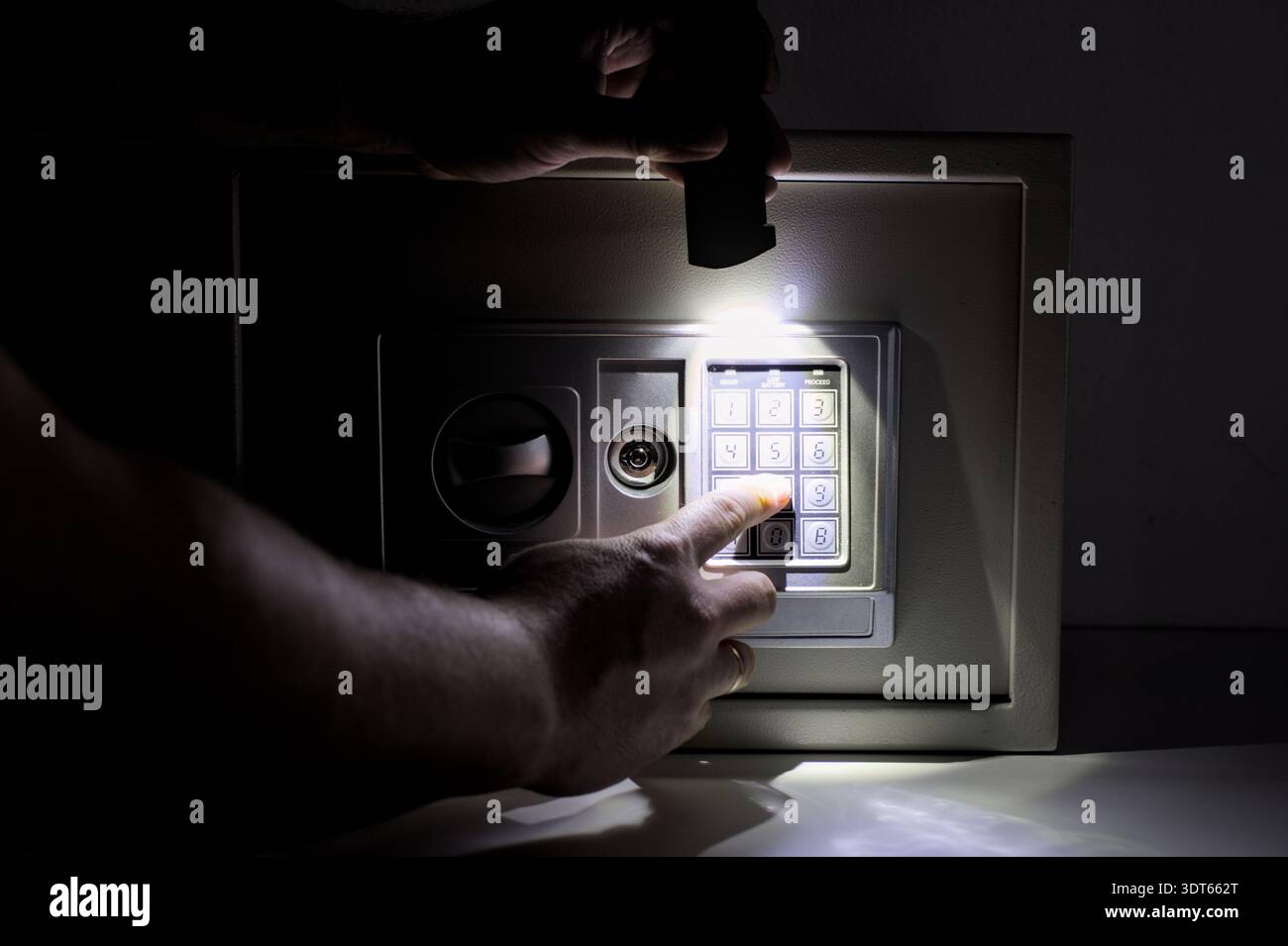 Uomo che inserisce il codice di sicurezza sulla cassetta di sicurezza elettronica in una stanza buia con torcia. Concetto di mistero, risparmi nascosti, sicurezza domestica e protezione finanziaria. Foto Stock