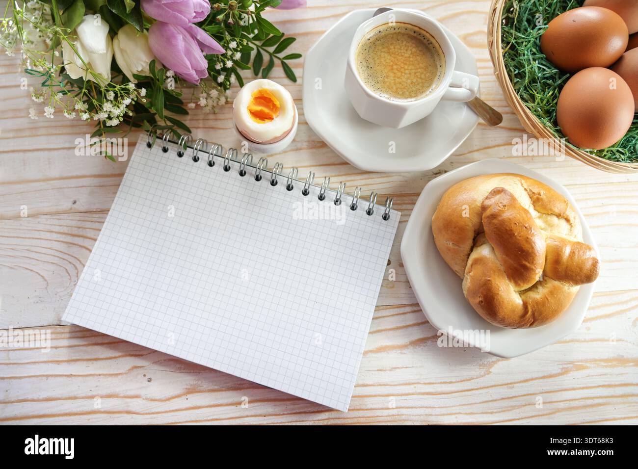 Blocco note a spirale a scacchi vuoto su un tavolo di Pasqua con uova, panini, fiori primaverili e caffè, mock-up per una lista delle cose da fare, invito o salvare la data, Foto Stock