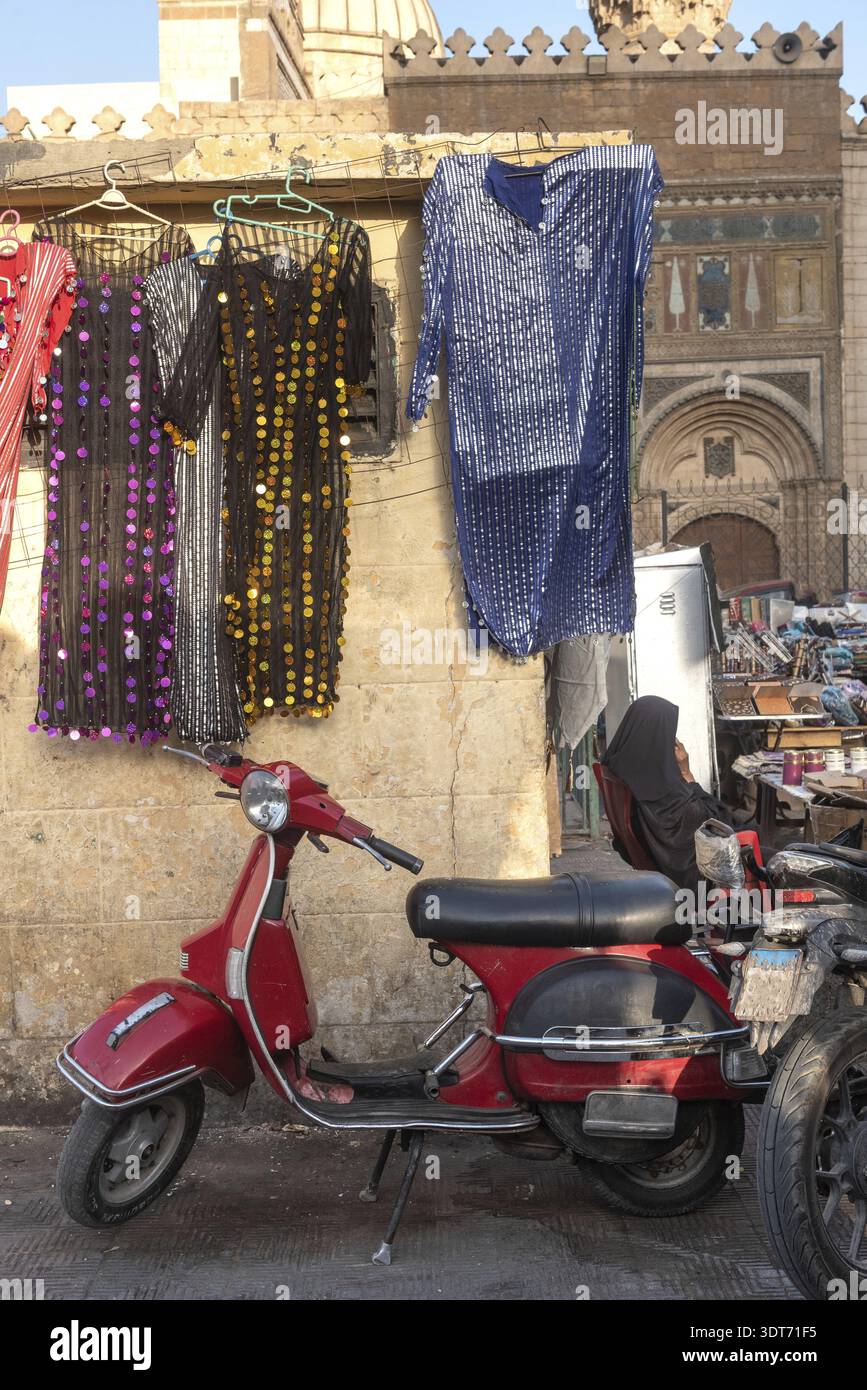 Uno scooter rosso dall'aspetto accattivante parcheggiato in un affollato mercato di strada che vende abiti da donna colorati vicino al famoso bazar Khan el Khalili, la storica California Foto Stock