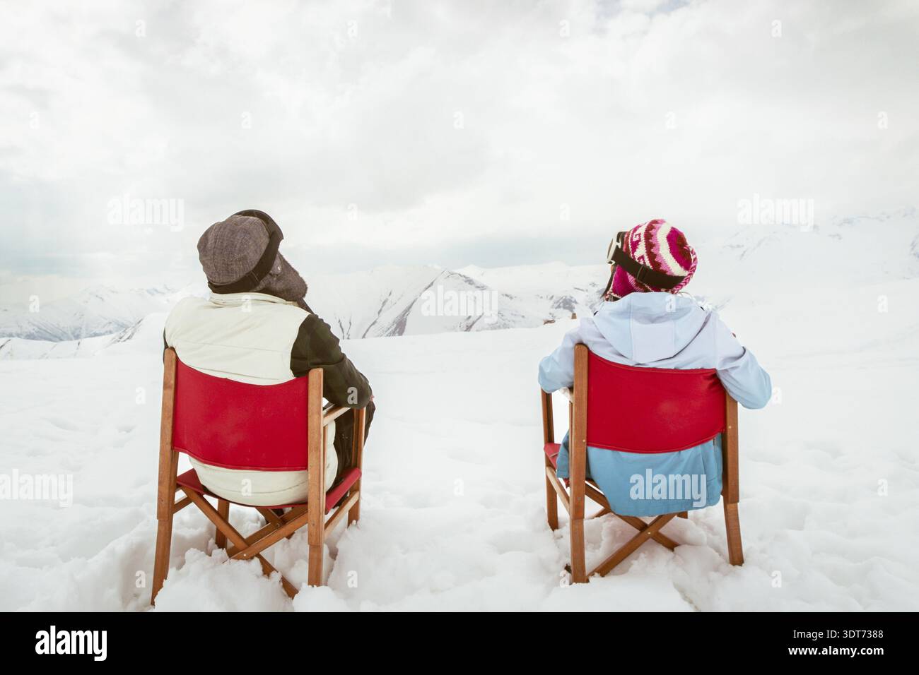 Coppia con vista sul retro seduto su sedie a sdraio vicino alla pista da sci, godendo della vista sulle montagne innevate del caucaso e del tempo libero invernale. Vacanze sciistiche a Gudauri, Georgia Foto Stock
