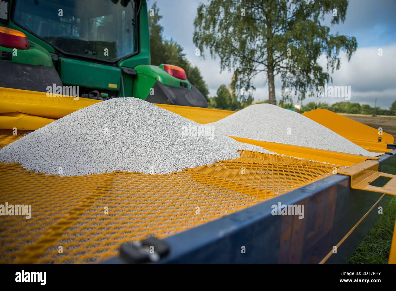 Primo piano di granuli di fertilizzante bianco caricati in uno spanditore agricolo collegato a un trattore. Attrezzature agricole di precisione per la preparazione di fertilizzanti per campi di coltura Foto Stock