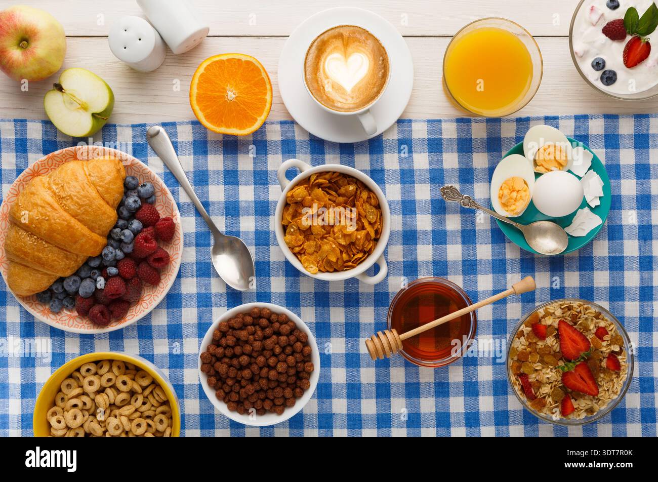 Una varietà di cibi per la colazione è organizzata su un panno a scacchi blu Foto Stock