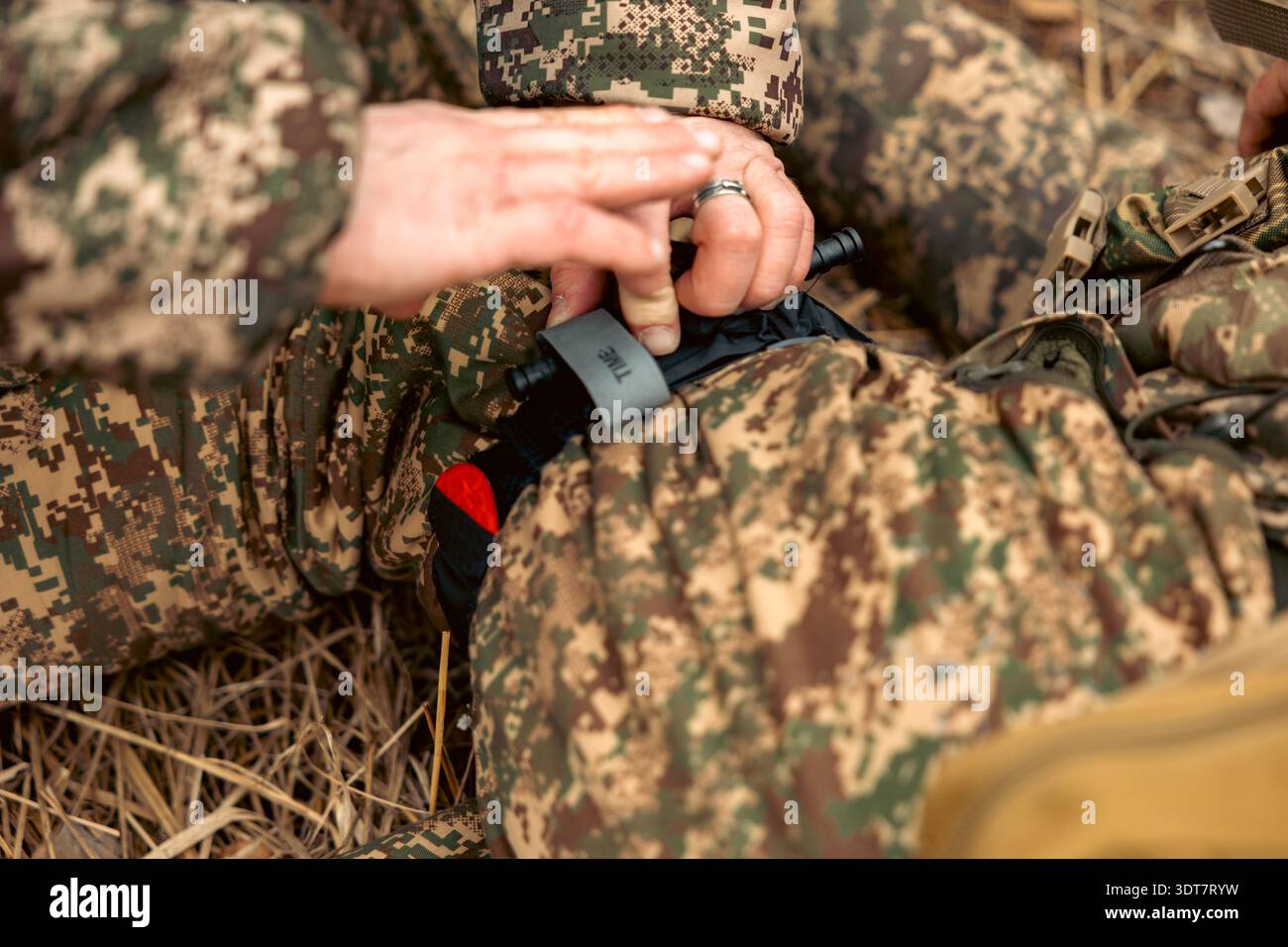 Tourniquet di emergenza applicato sui pantaloni mimetici. Applicare Tourniquet al soldato ferito. Foto Stock