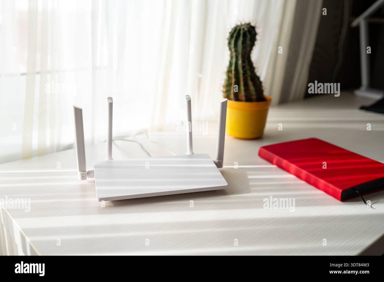 Moderno router wireless e personal planner rosso su un tavolo bianco con interni luminosi e minimalisti. Connessione Internet ad alta velocità, ufficio domestico e Foto Stock