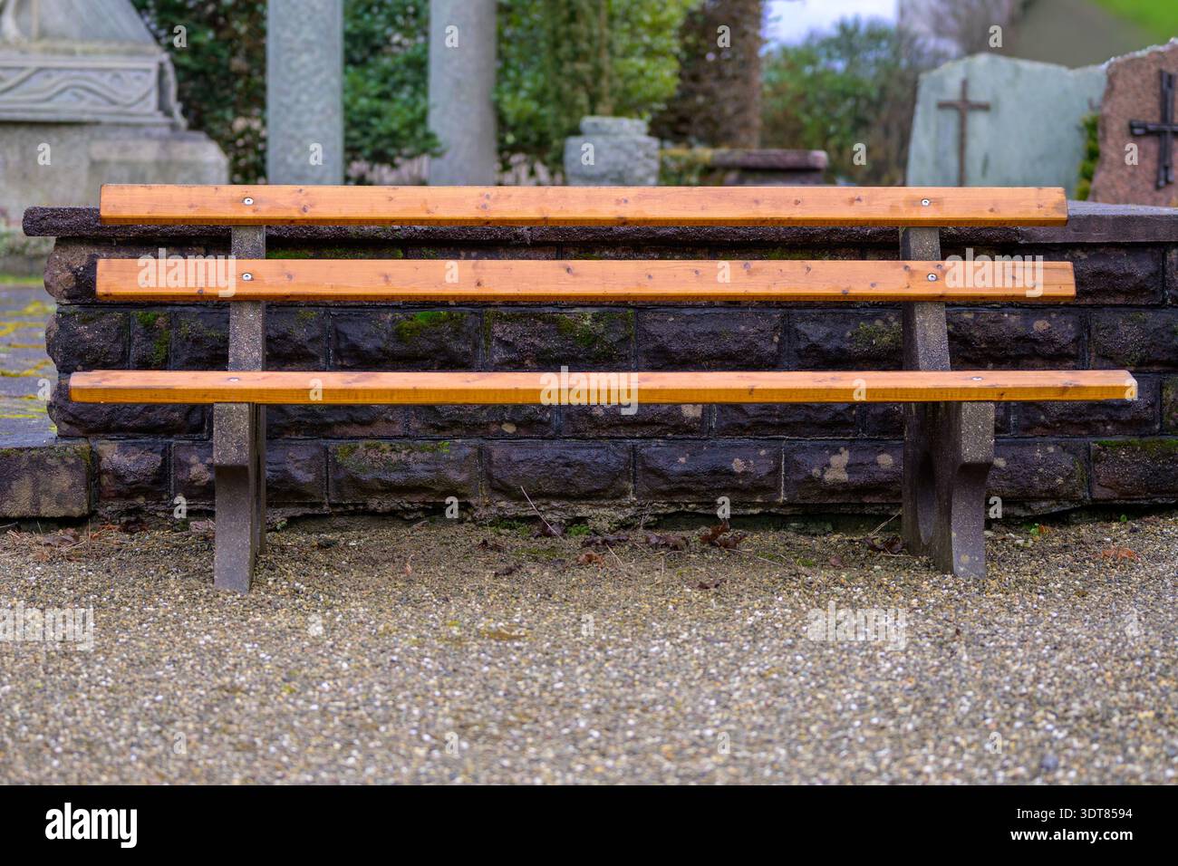 Panchina di legno vuota in un cimitero con lapidi sullo sfondo, che simboleggiano lutto, ricordo, dolore, perdita, riflessione e memoria pacifica. Foto Stock