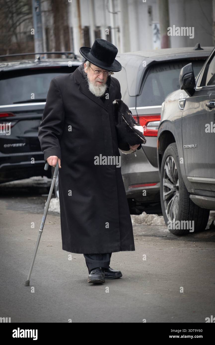 Un ebreo chassidico con un bastone attraversa la strada per partecipare ai servizi di preghiera mattutini. A Brooklyn, New York, inverno 2026. Foto Stock