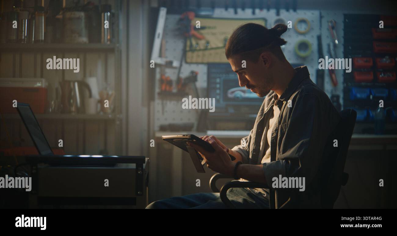 Specialista automobilistico maschio seduto in officina, che utilizza la configurazione a doppio schermo con laptop per fare riferimento incrociato ai dati del motore durante l'ispezione approfondita del veicolo. Concetto di soluzioni diagnostiche intelligenti. Foto Stock