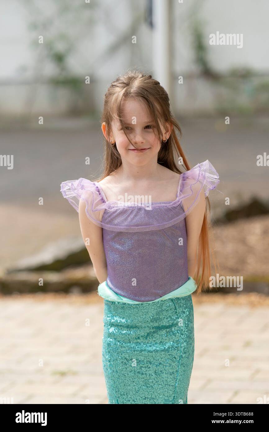 Una ragazza allegra che indossa un costume da sirena che posa all'aperto con le mani dietro la schiena e sorride alla telecamera. Immagine verticale. Concetto di infanzia Foto Stock