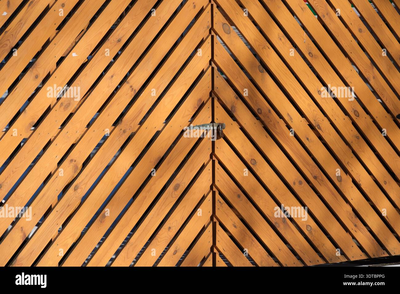 Un vivace cancello in legno mostra linee diagonali audaci sotto la luce del sole. Foto Stock