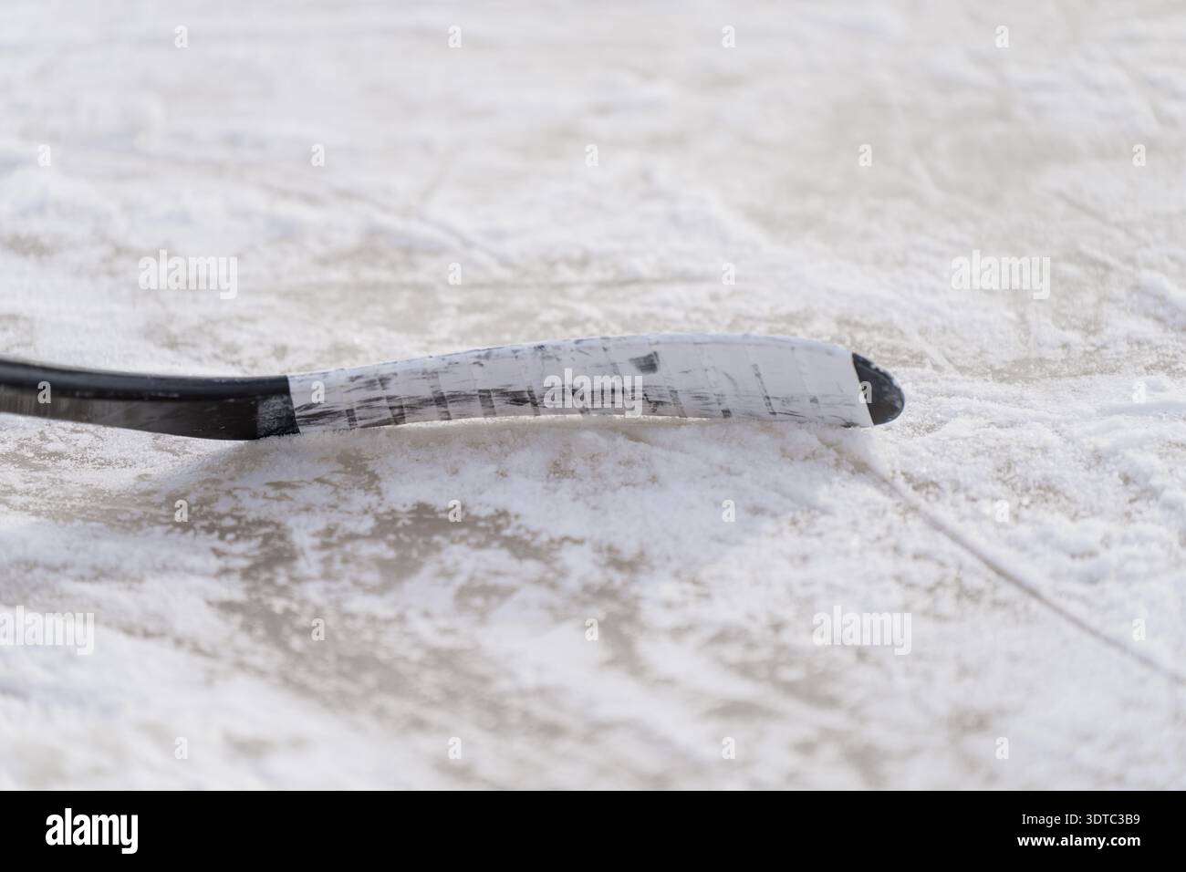 Lama di bastone da hockey poggiata su ghiaccio ghiacciato con segni di pattinaggio e neve in polvere, sfondo sportivo minimo per gare, allenamento e tematica di squadra Foto Stock