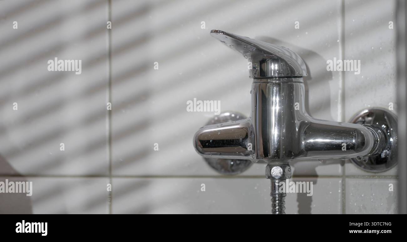 Rubinetto d'acqua con motivi luminosi e ombrosi in bagno durante il giorno Foto Stock