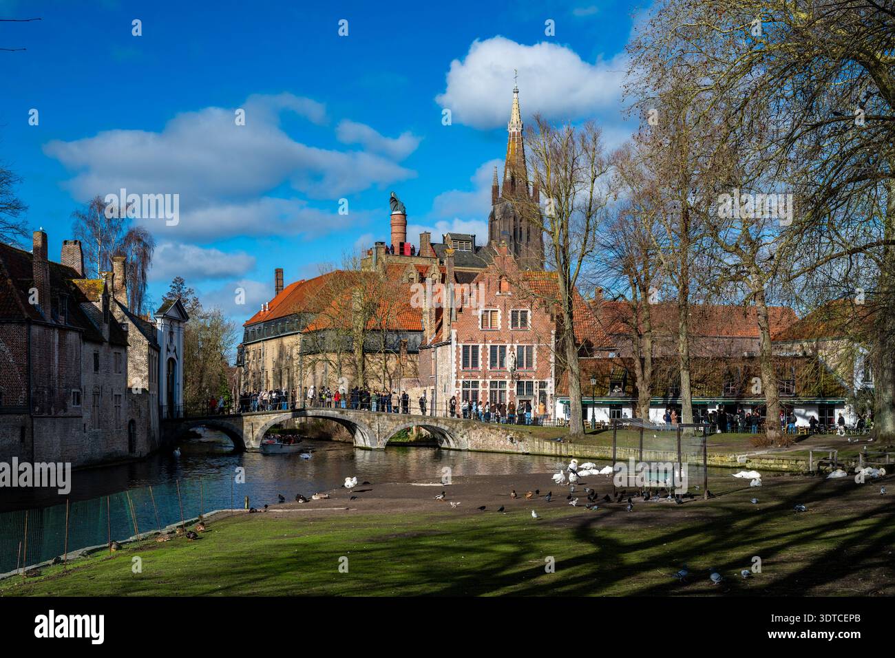 Bruges, Belgio - 14 febbraio 2026: I visitatori attraversano il ponte vicino a Begijnhof e Wijngaardplein con la torre della Chiesa di nostra Signora che sorge in istoria Foto Stock