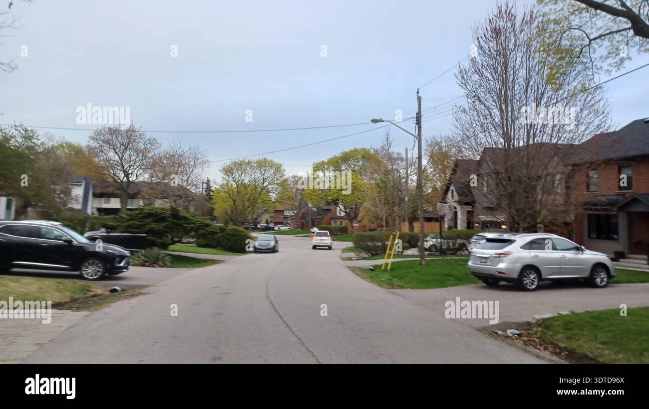 Toronto, ON, Canada - 26 aprile 2025: Una strada a Etobicoke mostra l'atmosfera suburbana con auto e alberi in erba. Foto Stock