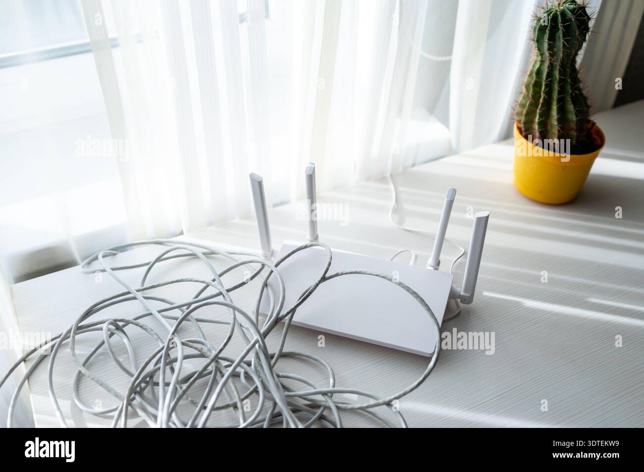 Router wireless moderno su un tavolo con una pila di cavi patch di rete grigi in un interno soleggiato. Concetto di installazione di reti domestiche, gestione dei cavi, Foto Stock