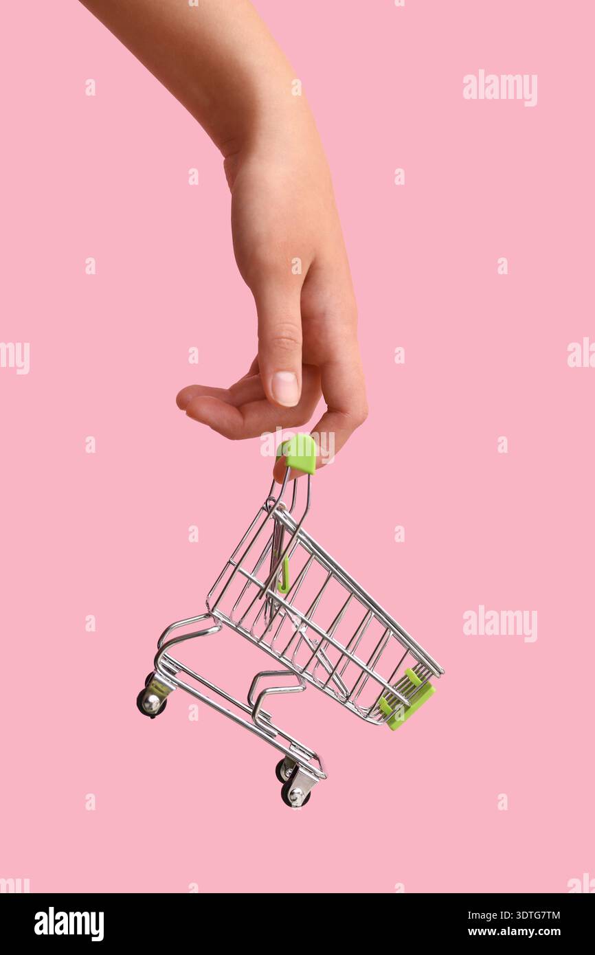 Mano femminile con carrello verde su sfondo colorato. Foto Stock