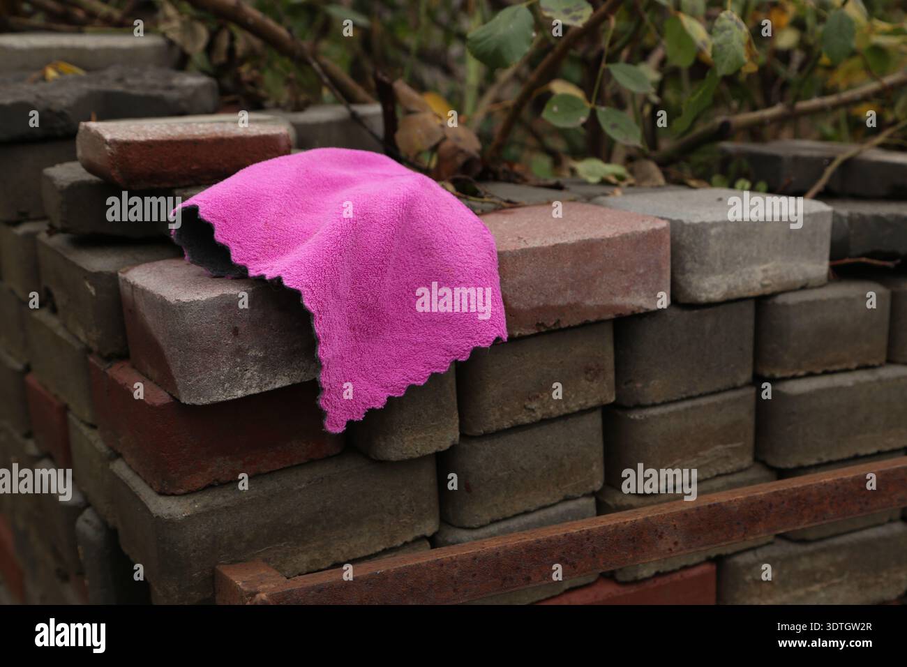 Un panno rosa giace su una pila di mattoni in un giardino. I mattoni sono disposti in vari colori e l'area mostra un po' di verde. E' giorno. Foto di alta qualità Foto Stock