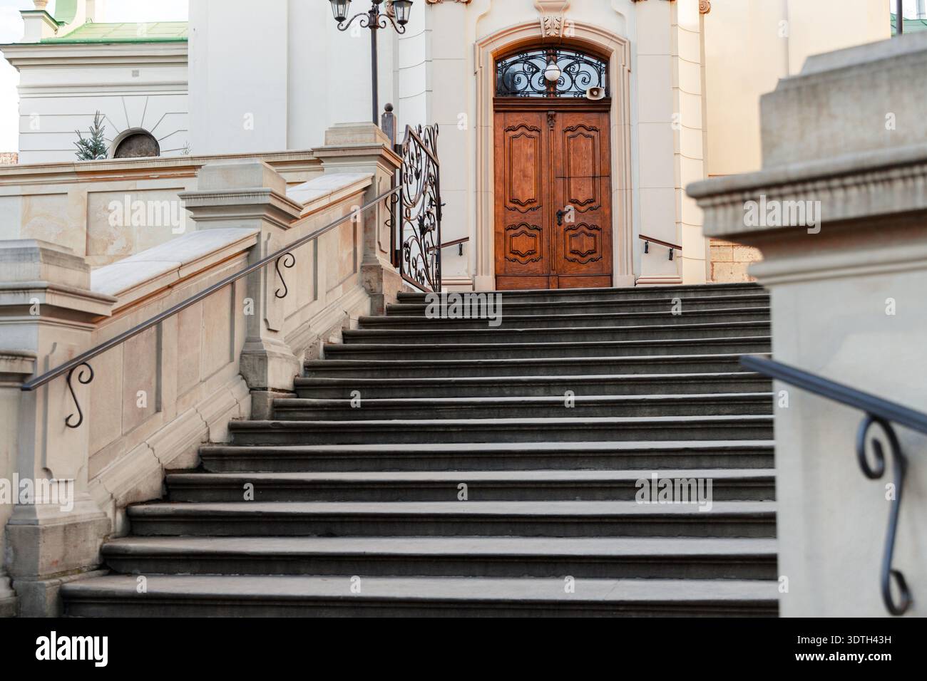 Un'ampia scalinata in pietra intemprata con ringhiere decorative sale verso una porta doppia in legno antico splendidamente lavorata all'interno di una entr ad arco Foto Stock