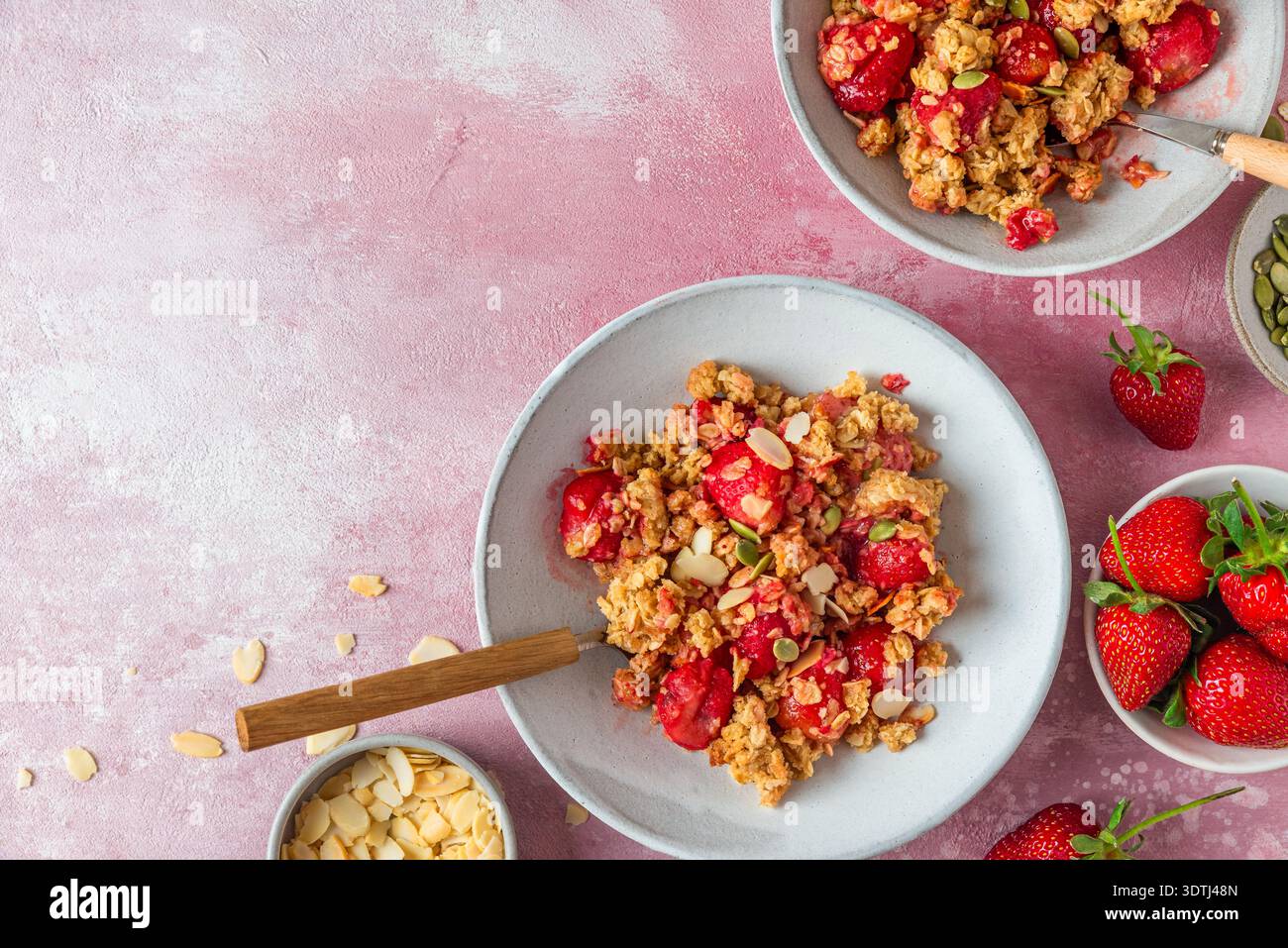 Dessert crumble alla fragola con granola al forno, semi di zucca e scaglie di mandorle in ciotole su sfondo rosa con spazio per copiare. Pasta dolce fatta in casa con Foto Stock