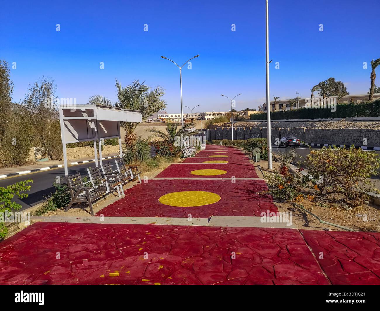 Marciapiede in cemento dipinto di rosso e giallo sulla strada per il vecchio mercato di Sharm El Sheikh (Egitto). Strada cittadina con panchine e palme Foto Stock
