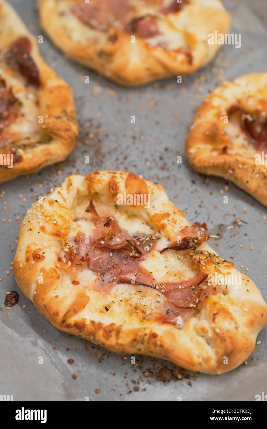 Mini pizzette di prosciutto e formaggio fatte in casa disposte su un vassoio da forno, spuntini italiani appena sfornati con formaggio fuso e crosta croccante. Focu selettiva Foto Stock