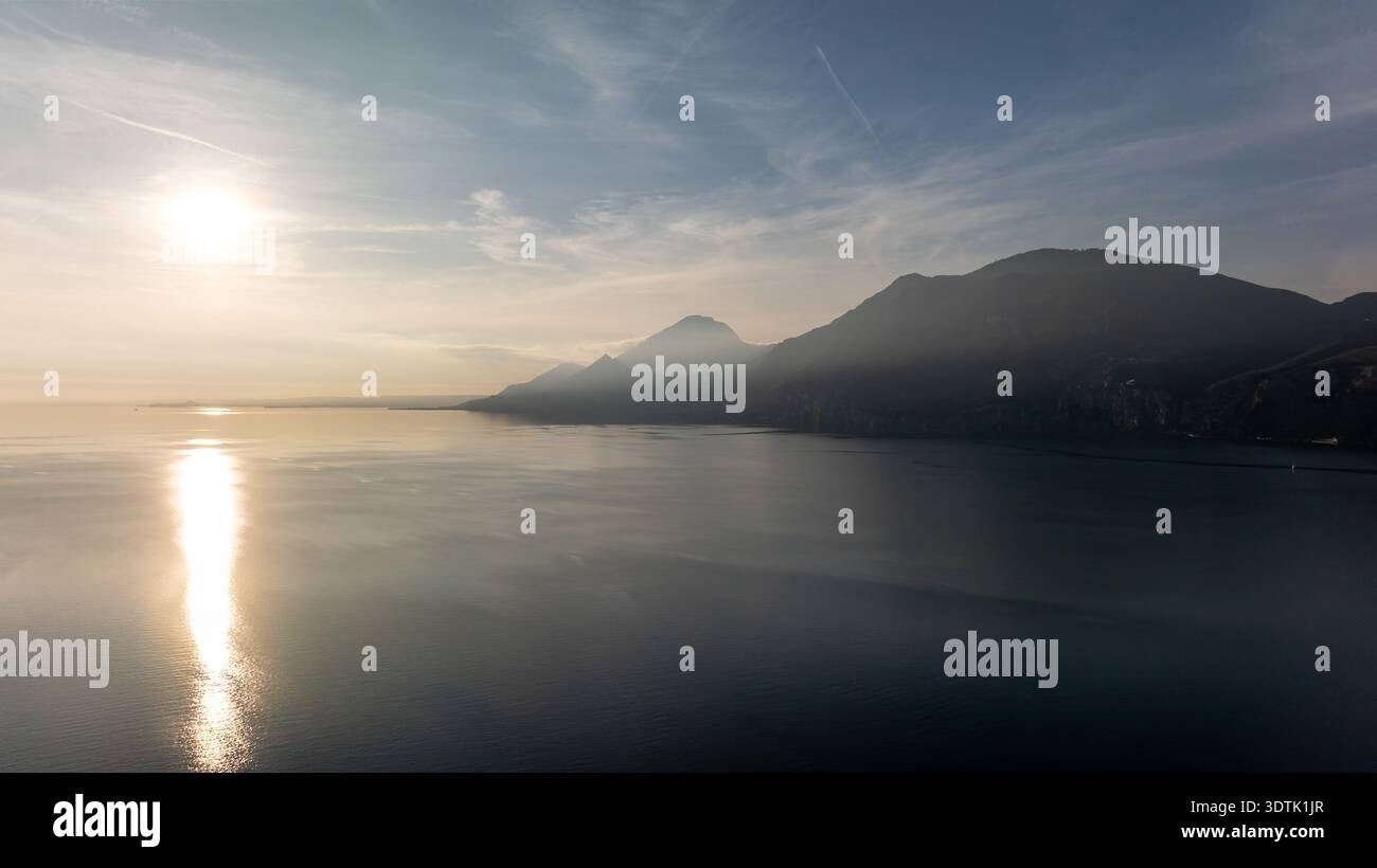 Una serena vista serale del Lago di Garda con il sole che tramonta sulla zona di Brenzone, che emette un caldo bagliore e si riflette sulle tranquille acque del Nord Foto Stock