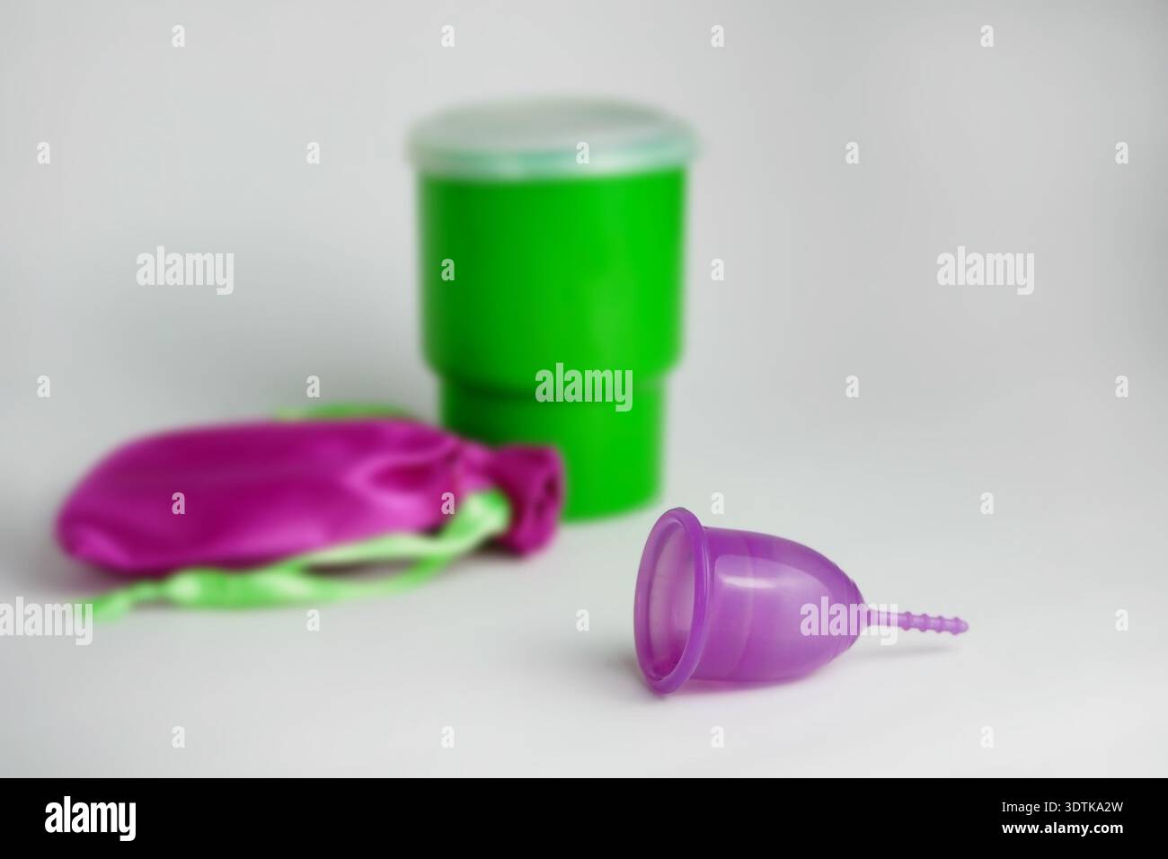 Tazza mestruale viola appoggiata su una superficie pulita con un contenitore verde e una custodia rosa, per un'igiene sostenibile. Foto Stock